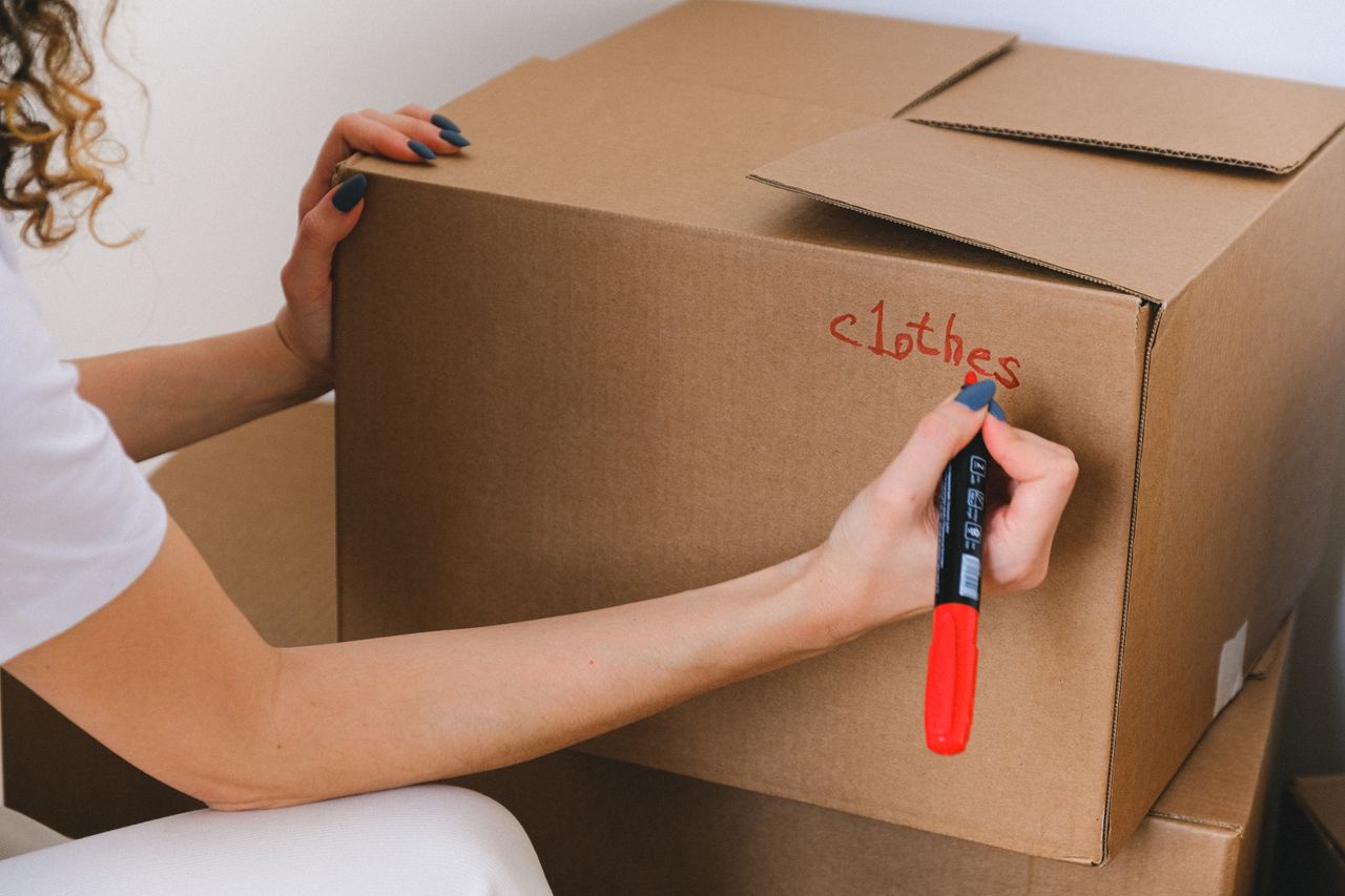 services-02 Close-up of a woman labeling a cardboard box with a red marker indoors.